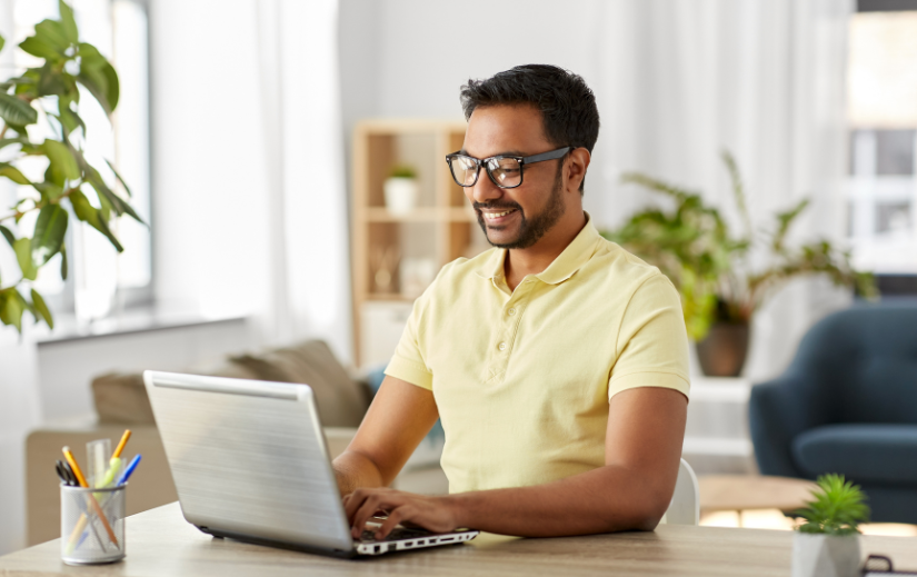 Smiling man in glasses working on a laptop at home, representing business growth strategies in a remote work setting.